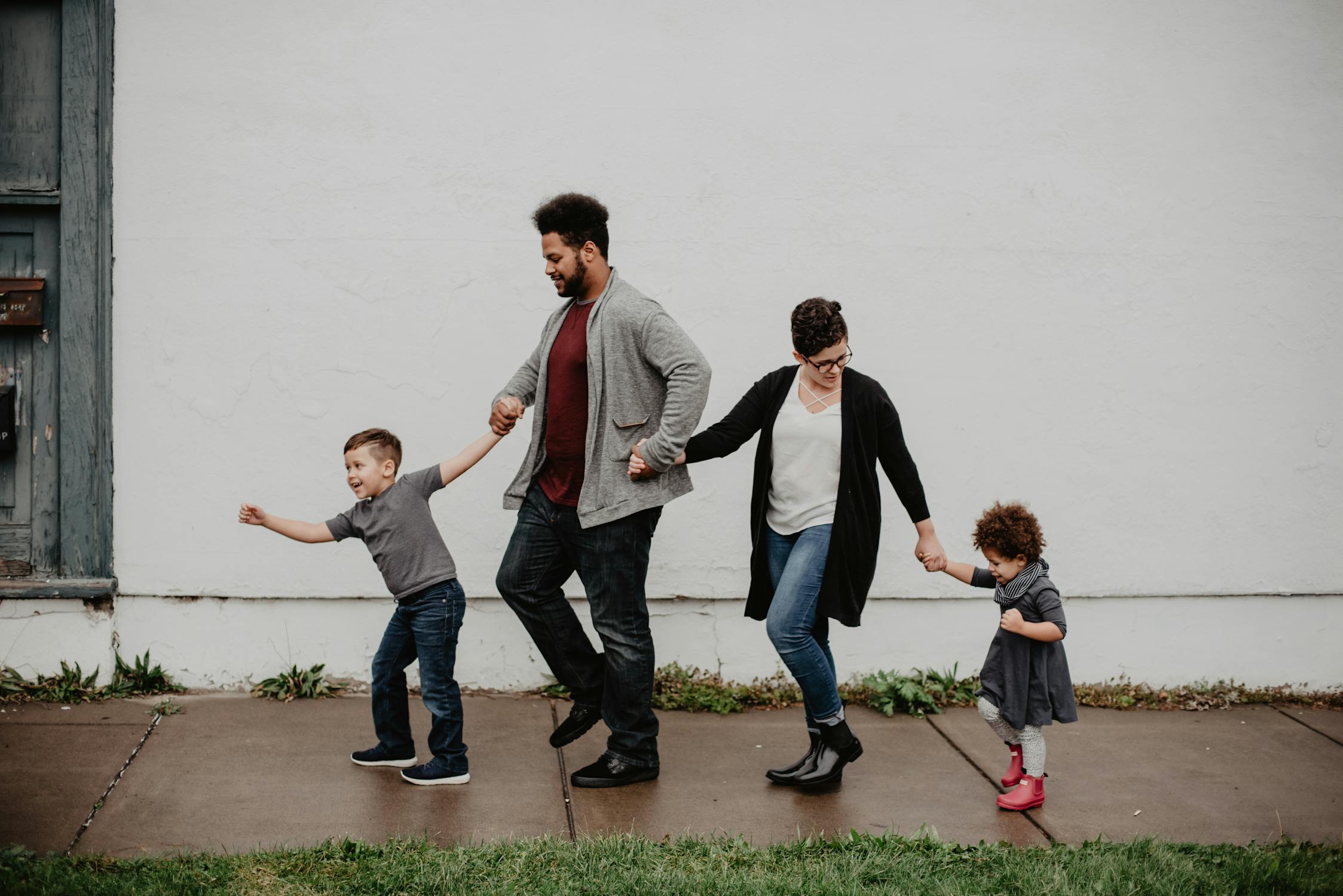 Parents walking hand-in-hand with their two young children on a sidewalk, reflecting the partnership and shared responsibility that makes life insurance conversations important for families